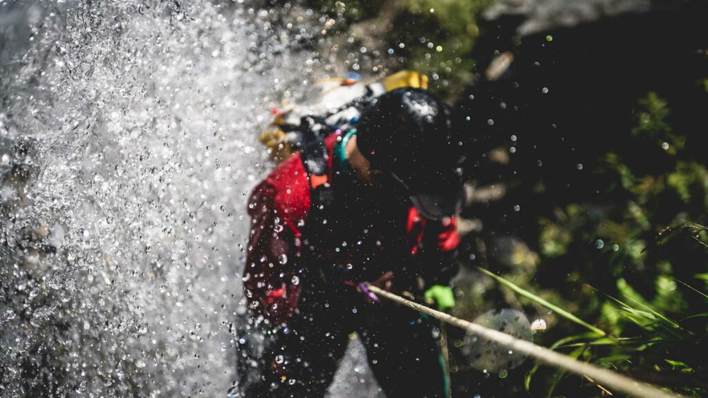 A canyoner rappeling in a white water splash waterfall